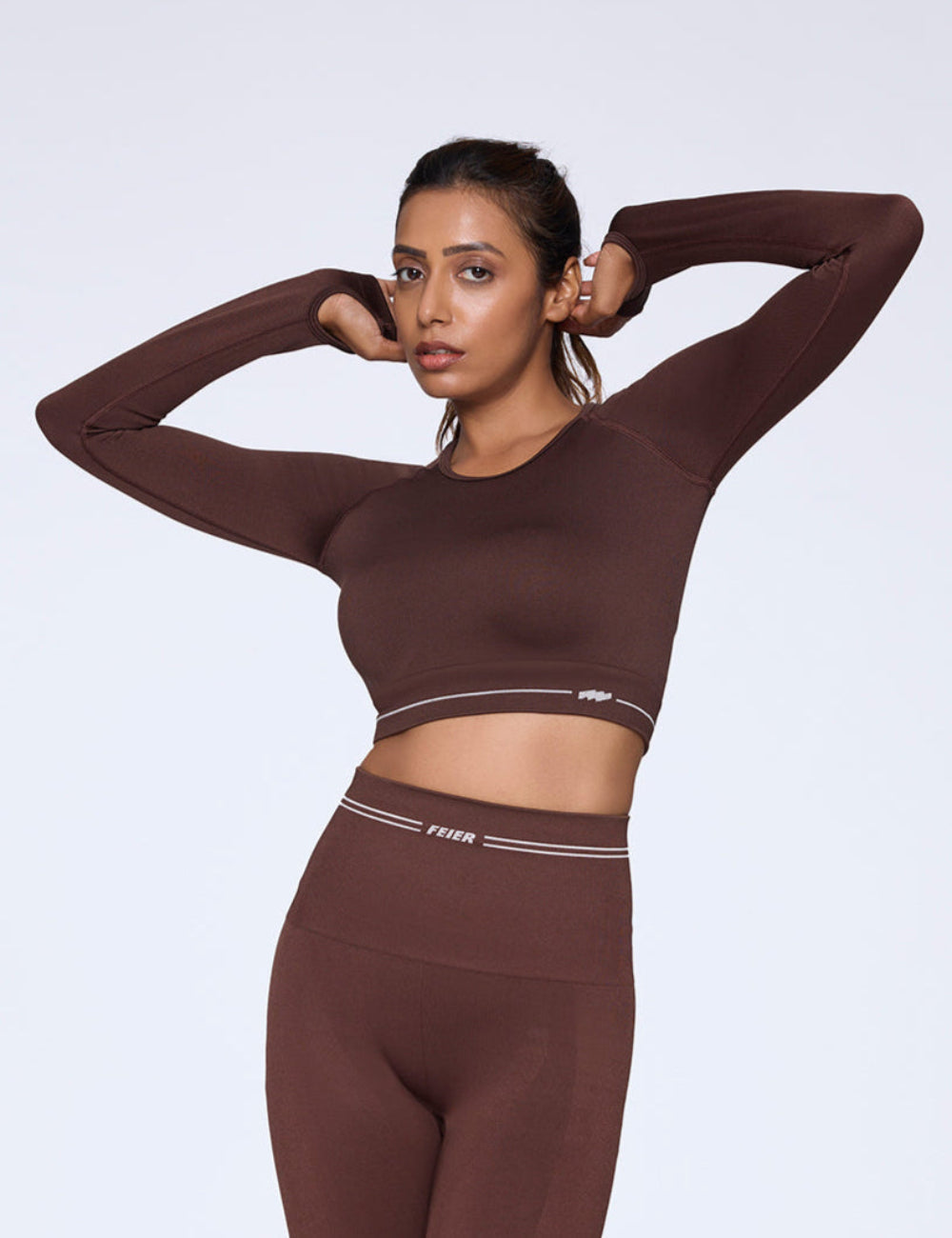 Woman wearing a brown athletic outfit with a visible brand logo on a white background