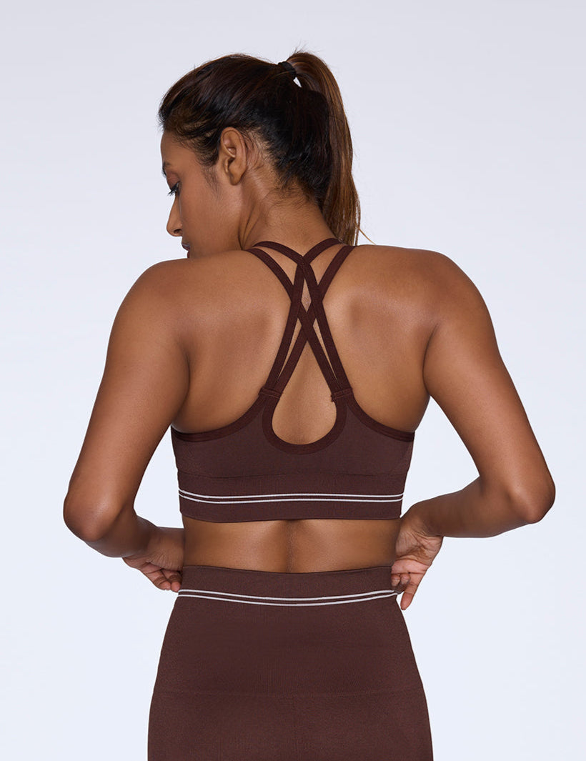 Woman wearing a strappy brown sports bra with her back to the camera on a white background