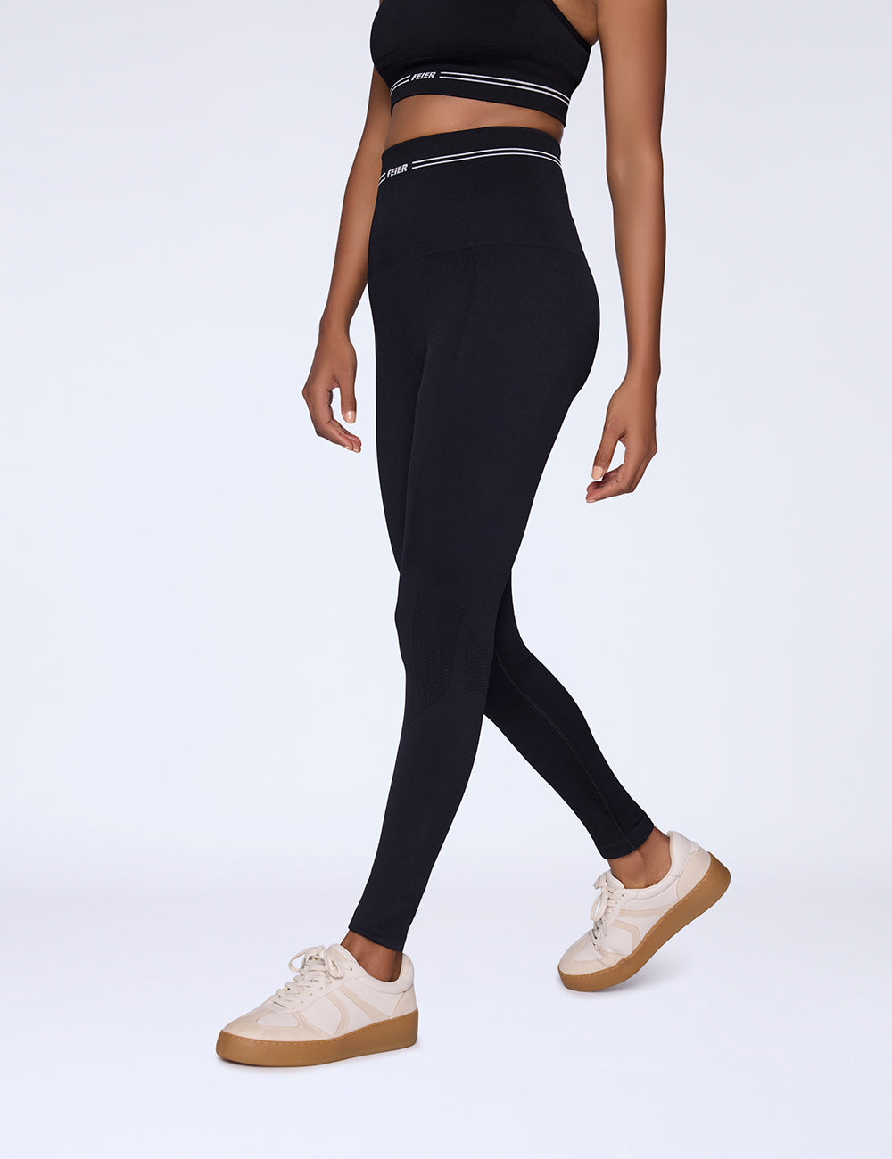 Woman wearing black leggings and a black crop top on a white background