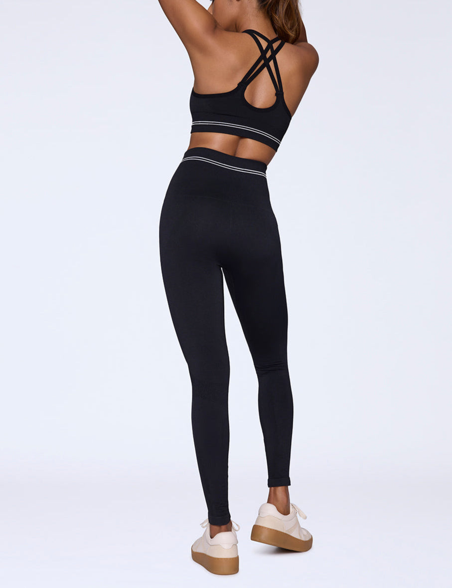 Woman wearing a black sports bra and leggings set on a white background facing away from the camera